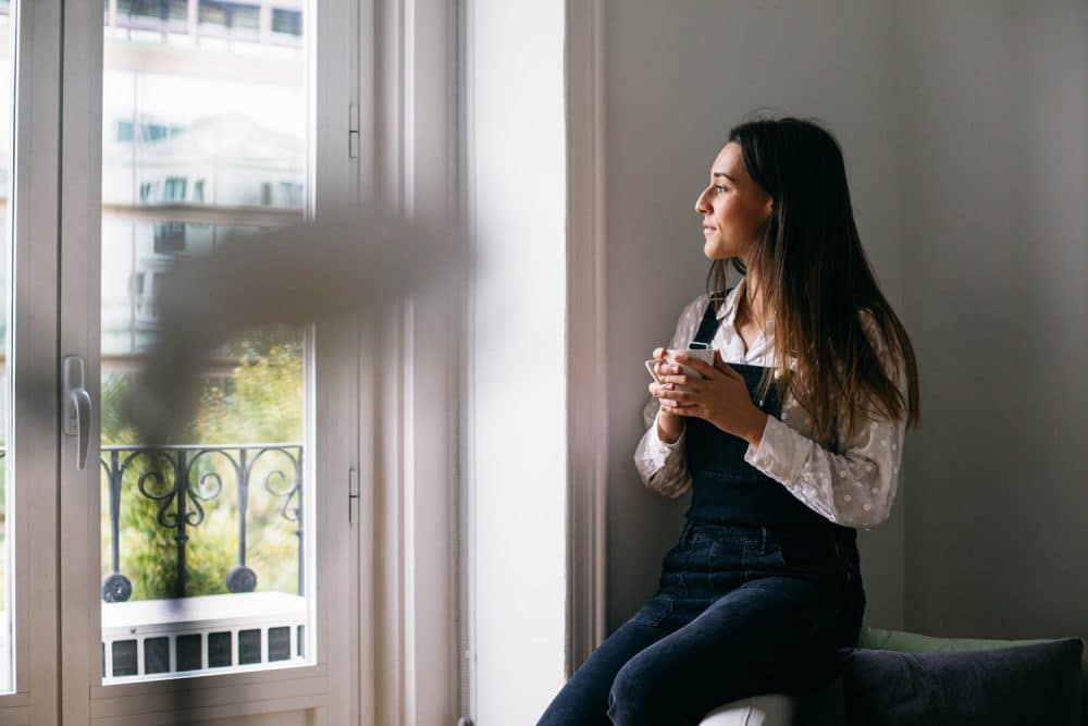 Thoughtful businesswoman looking through window while having coffee at office